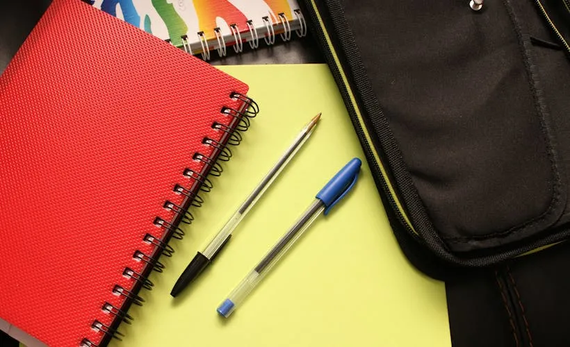 Black and Blue Pens Beside Red Covered Notebook